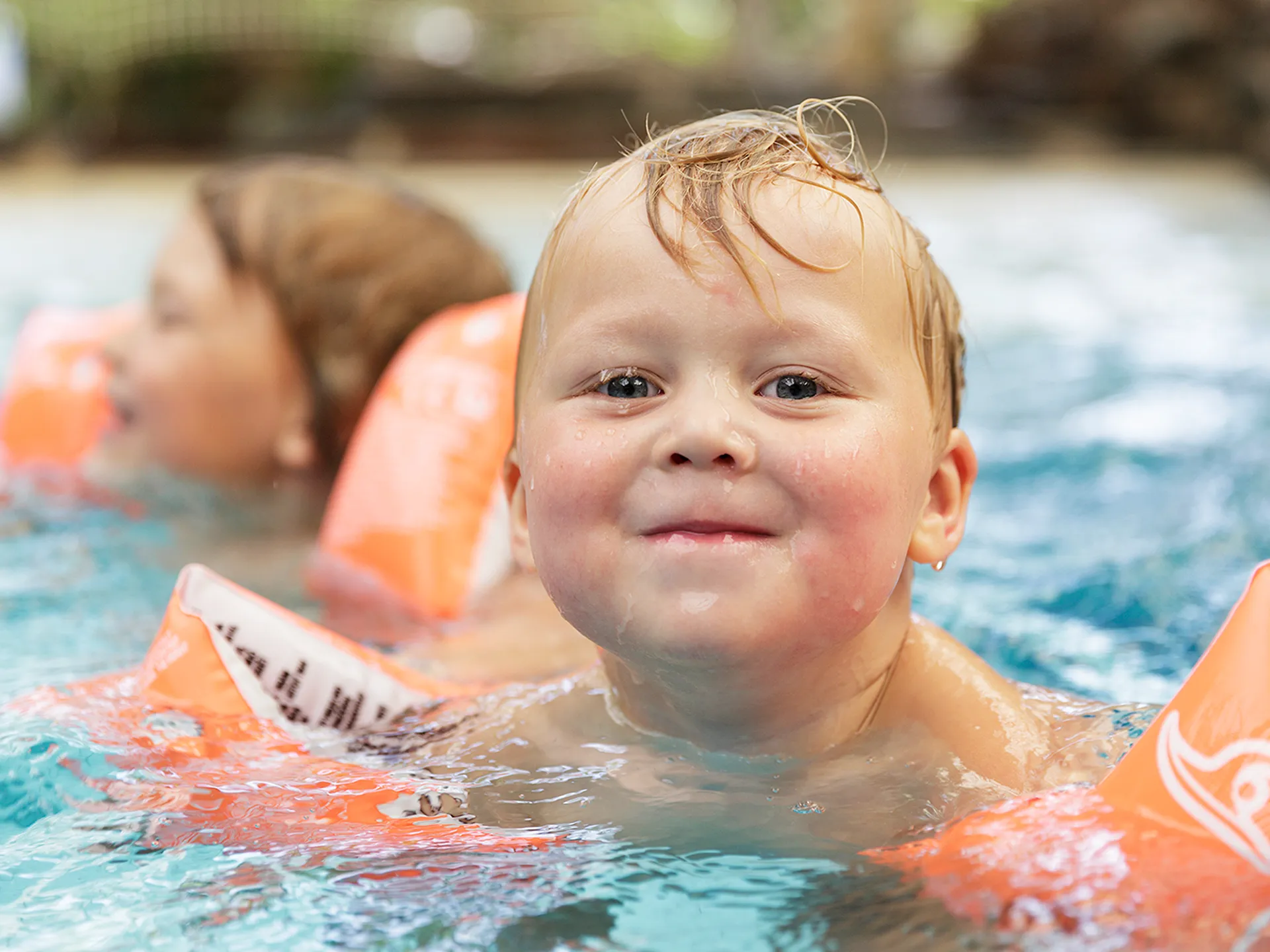 Lachend kind met oranje bandjes in het water van Center Parcs Het Meerdal.