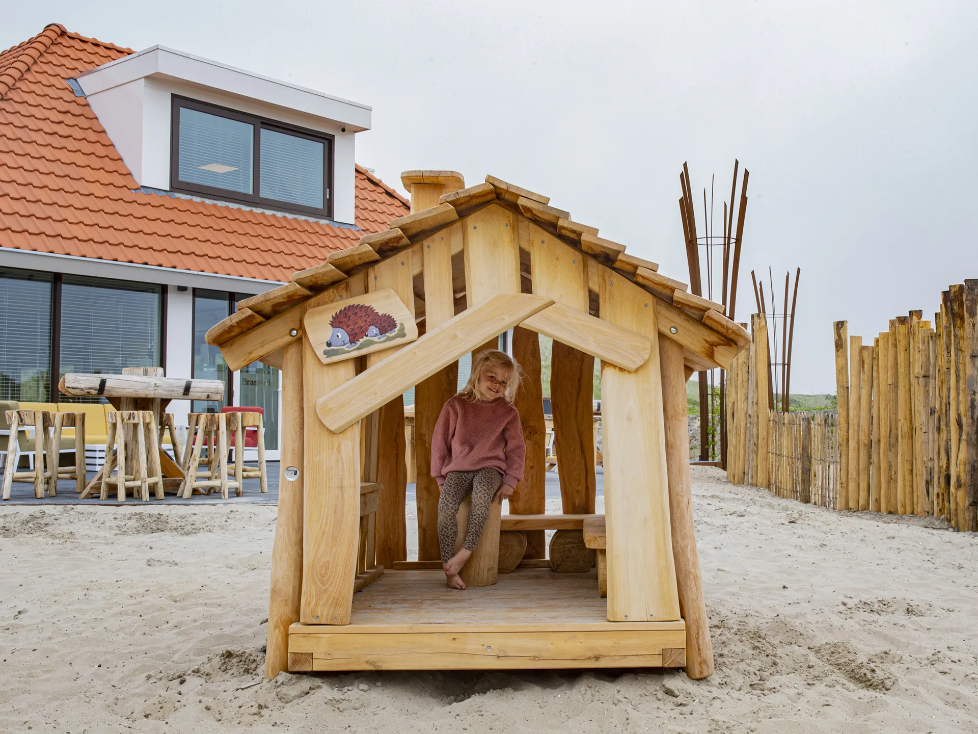 Spelend kind in een houten speelhuisje op het zand van het kindvriendelijke vakantiepark Landal Callantsoog.