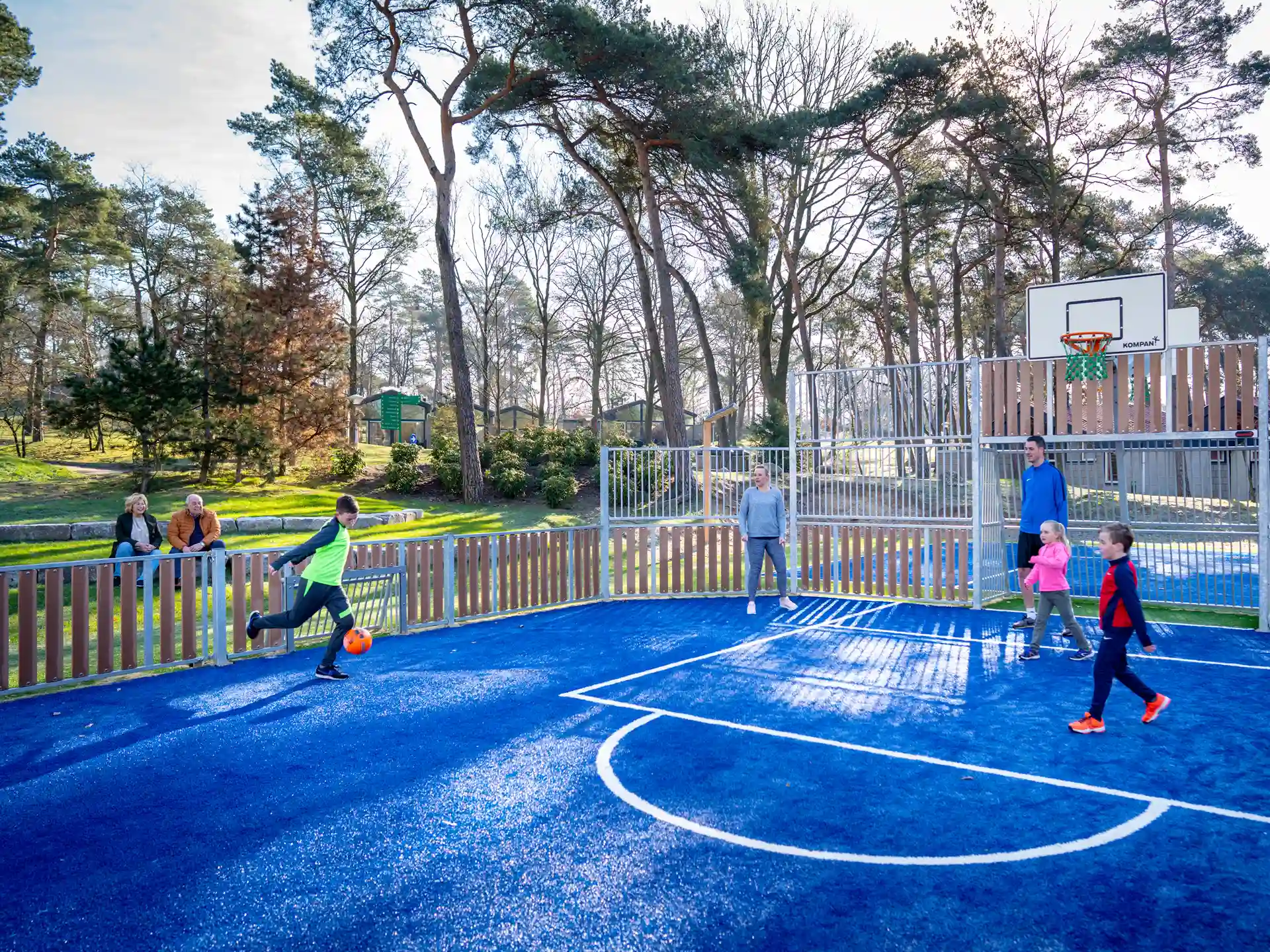 Een gezin voetbalt op het blauwe multifunctionele sportveld van Landal De Lommerbergen.